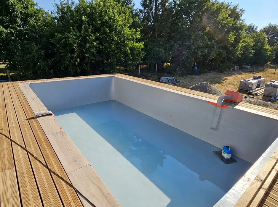 Piscine rectangulaire neuve en cours de remplissage, terrasse en bois composite IPE, liner gris clair, mains courantes inox