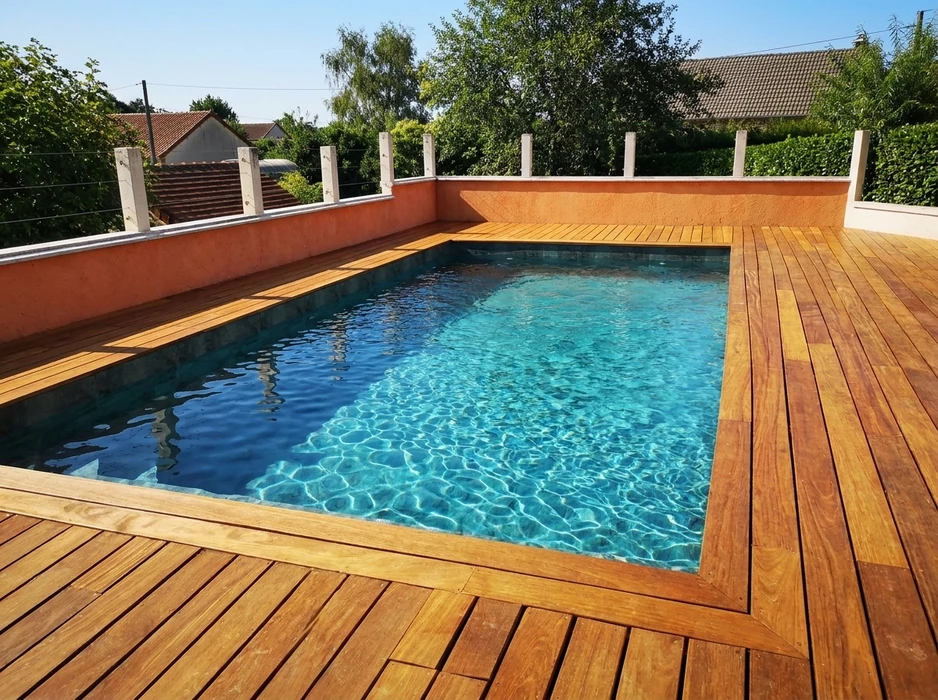 Terrasse extérieure avec piscine rectangulaire encastrée, entourée d'un deck en bois massif type ipé ou teck, lames posées perpendiculairement au bassin