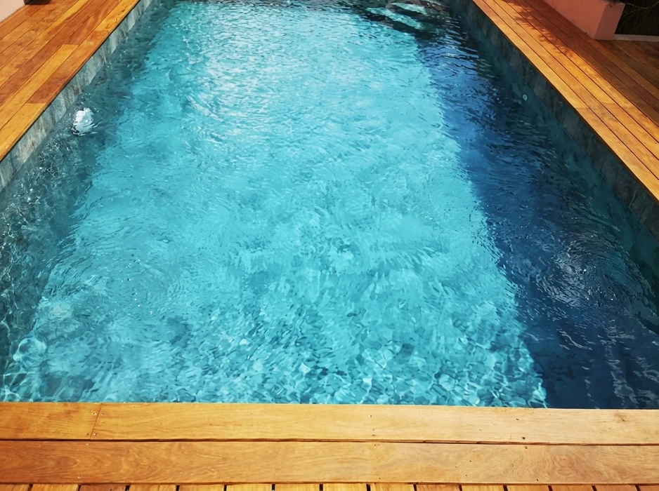 Piscine rectangulaire extérieure aux eaux turquoise cristallines, entourée d'une terrasse en bois exotique (type ipé)